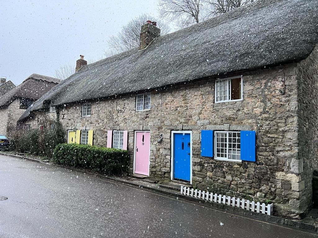 snow falling over Honeysuckle thatched Cottage in West Lulworth, Dorset